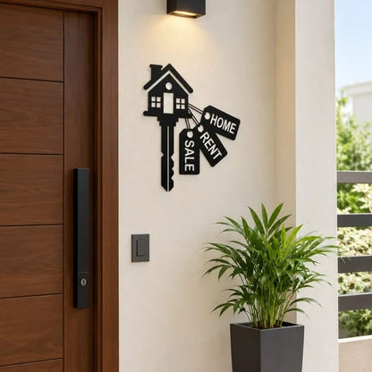 Black house key wall sticker with Home, Rent and Sale tags mounted on a cream wall beside a wooden entrance door.