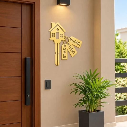 Black house key wall sticker with Home, Rent and Sale tags mounted on a cream wall beside a wooden entrance door.